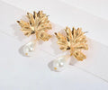 A pair of gold leaf-shaped drop earrings with teardrop pearl pendants, displayed on a clean white surface.