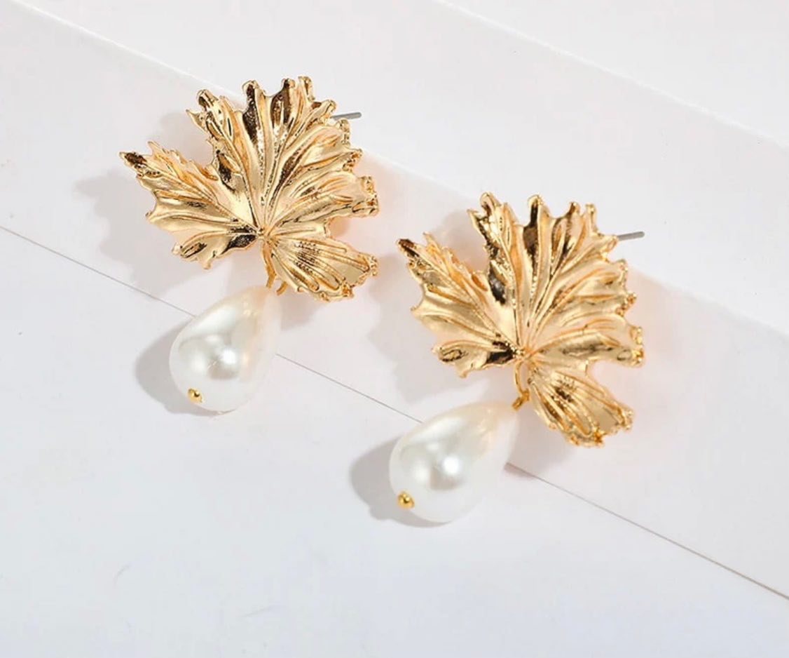 A pair of gold leaf-shaped drop earrings with teardrop pearl pendants, displayed on a clean white surface.